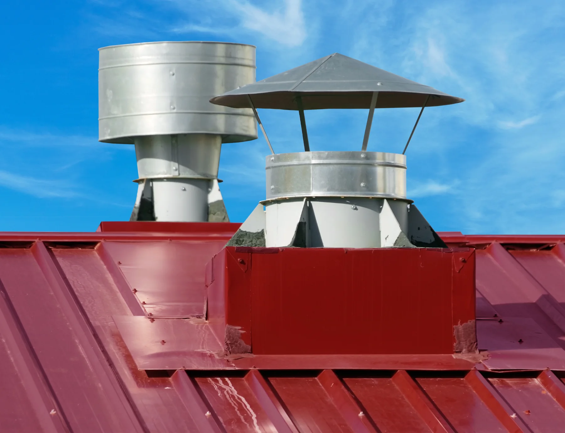 Ventilationshuvar och genomföringar på ett rött plåttak Ventilationshuvar och genomföringar på ett rött plåttak